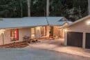 Modern house with large windows and a double garage in a wooded area at dusk.
