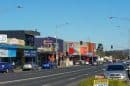 Main street in Boronia with shops, cars, and bus stops under a clear blue sky.