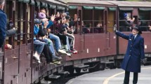 People boarding a vintage train at a station in a forested area in Victoria.