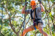 Person wearing helmet and harness crossing a high ropes course in a forest.