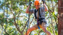 Person wearing helmet and harness crossing a high ropes course in a forest.