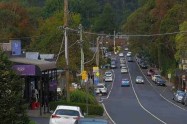 Main street in a mountain village with parked cars and shops, surrounded by forested hills.